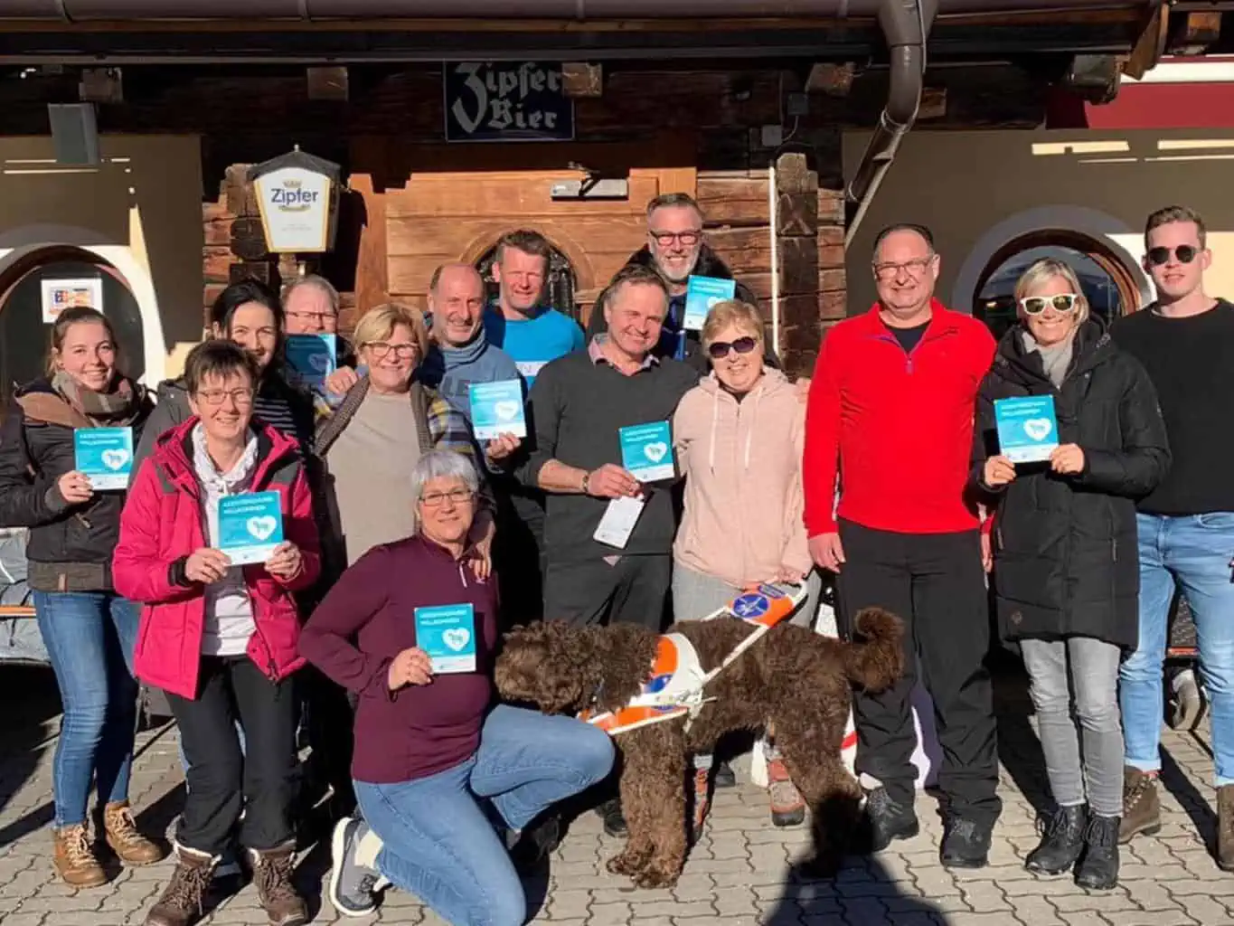 A group of enthusiastic people posing for a photo with a guide dog, each holding the label of the access campaign.