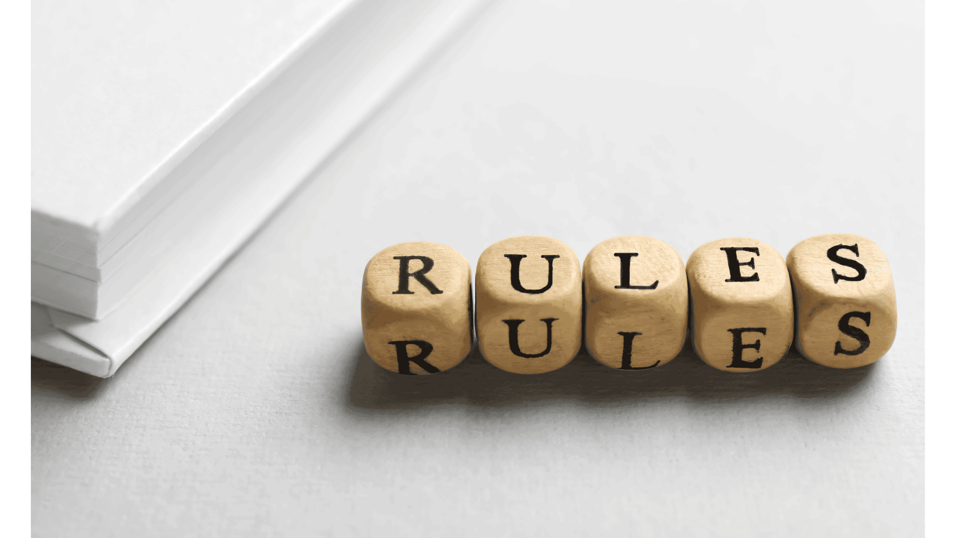 Wooden dice with black letters on it spelling "RULES"